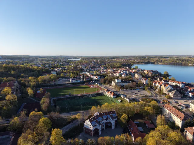 Panorama miasta z lotu ptaka, stadion z bieżnią, tereny zielone i jezioro.